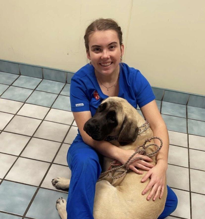 A student in scrubs poses with a dog on a tiled floor.